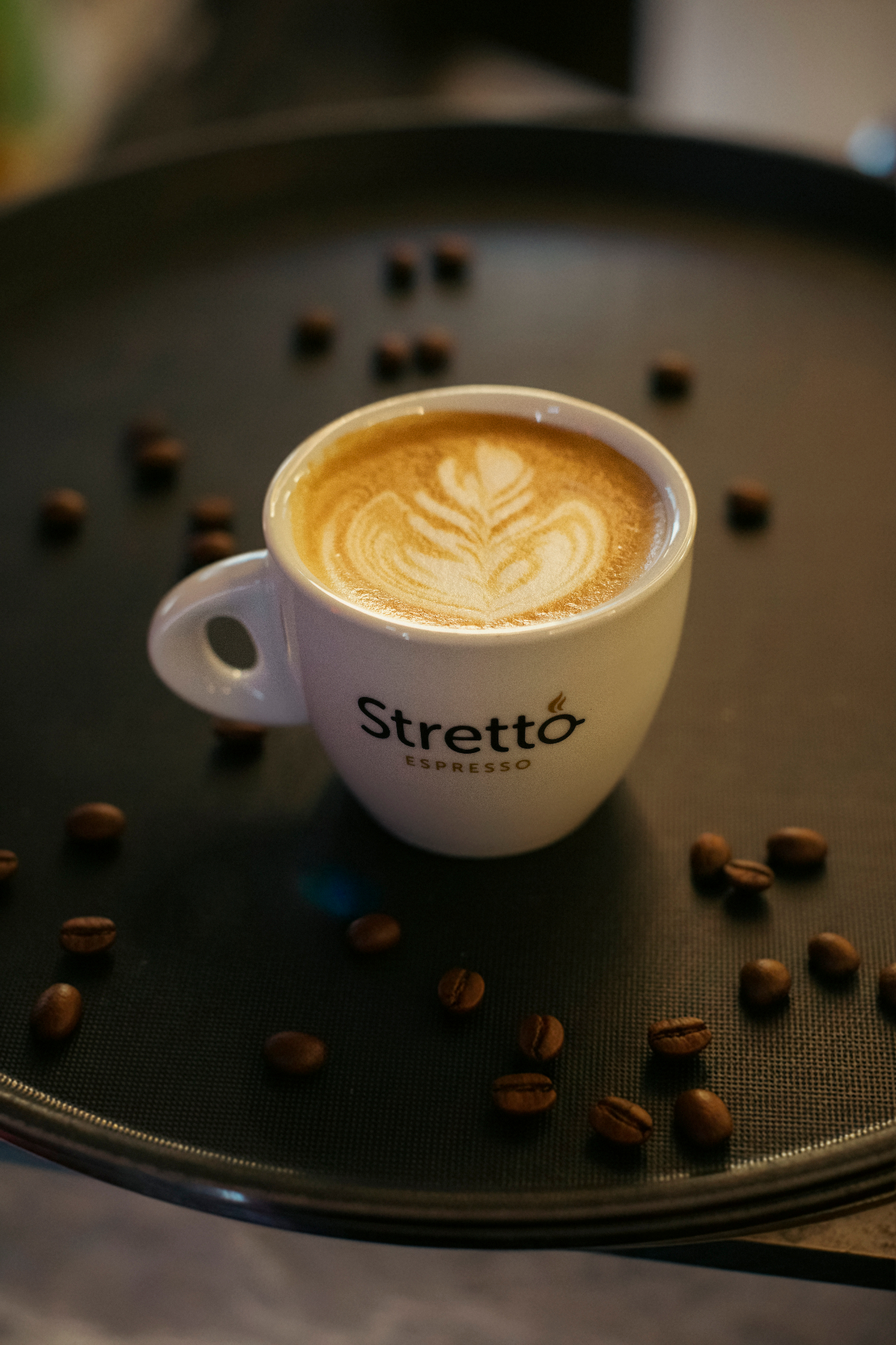 Espresso cup with latte art on a dark tray with coffee beans